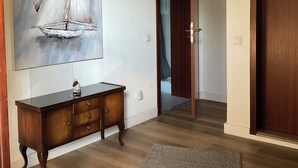 A hallway with a wooden floor, a dark wooden console table, a gray rug, and a large abstract painting of a sailboat on the wall. - Quiet, fully equipped guest apartment (Mettmann)