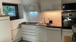 A modern kitchen with white cabinets, a built-in oven, and a window overlooking greenery. - Quiet, fully equipped guest apartment (Mettmann)