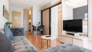 Una sala de estar moderna con un sofá gris, un televisor de pantalla plana y una zona de comedor con mesa y sillas.