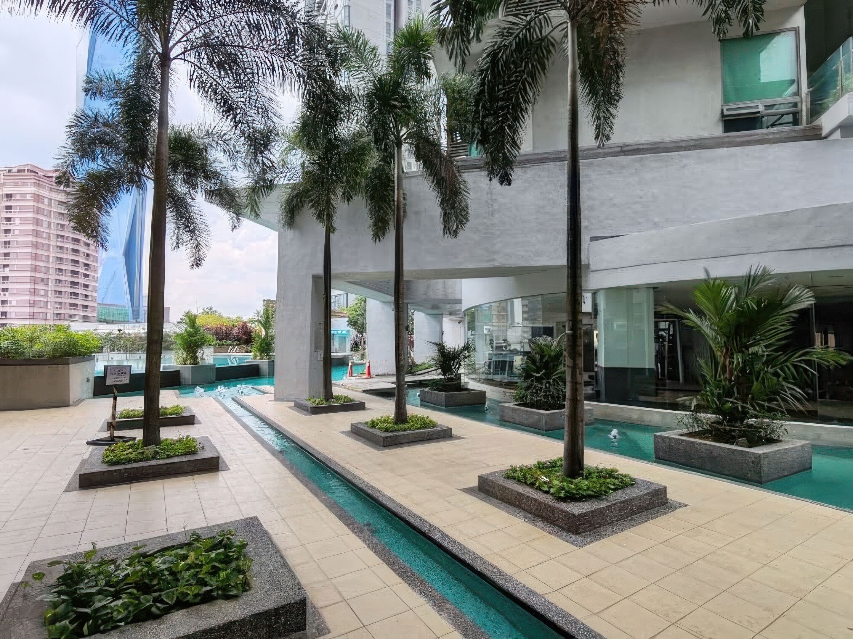 A modern indoor pool area with multiple pools, surrounded by palm trees and planters.