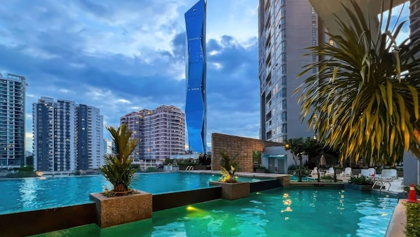 Zona de piscina en la azotea con vista a un edificio alto de forma peculiar y otros rascacielos circundantes.