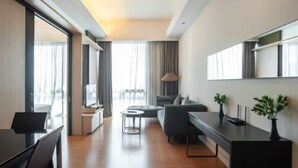 Habitación de hotel moderna con zona de comedor, sofá, escritorio y un amplio ventanal con cortinas.