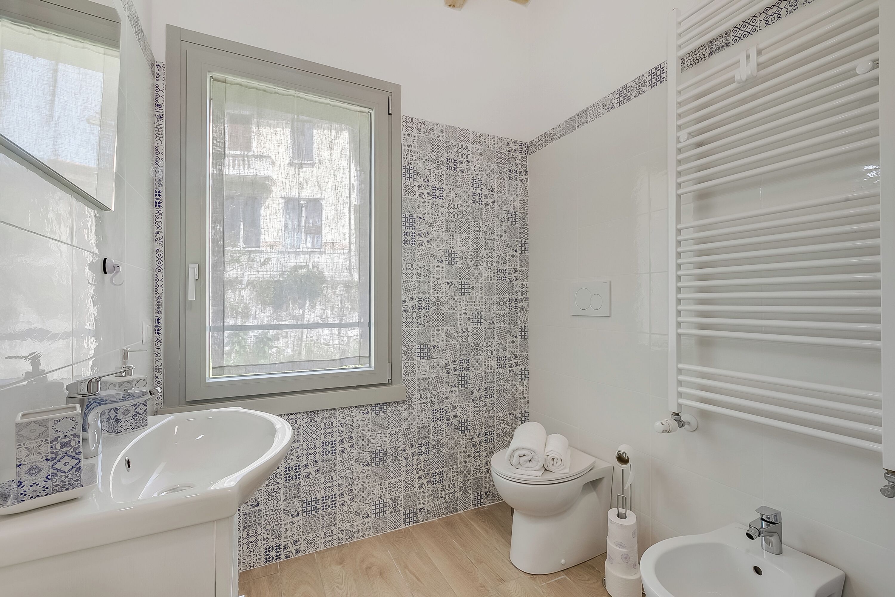 A bathroom with a sink, toilet, bidet, and a window.