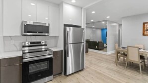 Una cocina moderna con electrodomésticos de acero inoxidable, un comedor con mesa y sillas, y una sala de estar con sofá y una pared azul de acento.