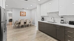 Una cocina moderna con comedor, que cuenta con encimera de mármol, electrodomésticos de acero inoxidable y armarios oscuros.