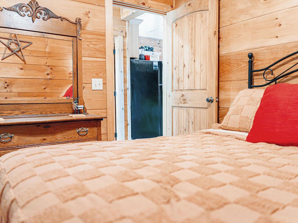 Ein Zimmer mit Holzboden, einem Bett, einer Kommode und einer Tür, die in einen Küchenbereich führt.