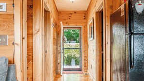 A wooden interior hallway with a black refrigerator on the right, a door leading outside, and a light fixture on the ceiling. - Long Valley Lights Cabin - Amazing View & 2 min. to the Blue Ridge Parkway (Fancy Gap)