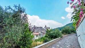 A stone-paved pathway leading to a historic building with a tower, surrounded by greenery and a clear sky. - Dimora Lucretili by Interhome (Tivoli)