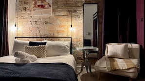 A hotel room with a brick wall, a bed with white linens, a small round table, and a chair. - Balmain Village Retreat | Sleeps 5 | AC + Parking | City 3kms (Balmain)