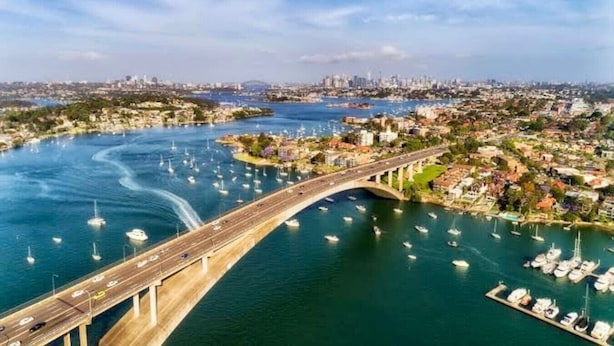 A coastal cityscape with a prominent bridge connecting two areas, a marina with numerous boats, and a distant city skyline. - Balmain Village Retreat | Sleeps 5 | AC + Parking | City 3kms (Balmain)