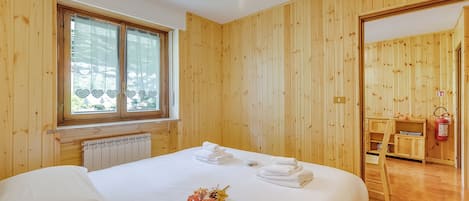 Habitación con paneles de madera, una cama, una ventana con cortinas con forma de corazón, un radiador y un extintor.