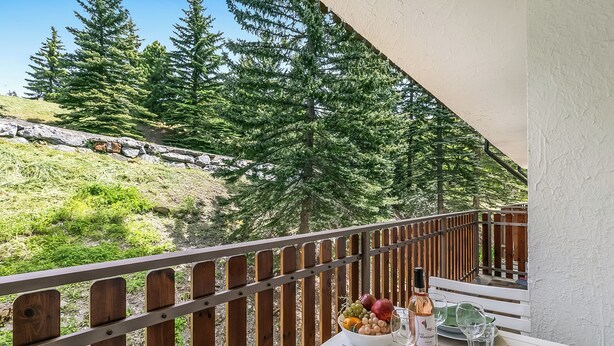 Un balcon avec une table dressée pour le dîner, donnant sur une colline boisée.