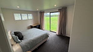 Ein Schlafzimmer mit einem Bett, einem Schreibtisch und Blick auf ein grünes Feld durch ein großes Fenster.