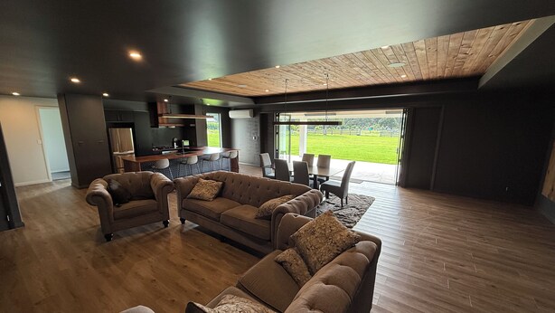 Ein modernes Wohnzimmer mit einer großen Eckcouch, einem Essbereich mit Tisch und Stühlen sowie einer Küche im Hintergrund.