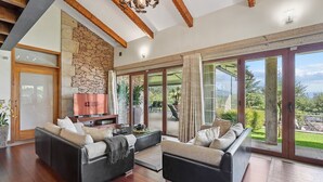 A spacious living room with a stone wall, wooden beams, and a large sliding glass door leading to an outdoor area. - GuestReady - Relaxing experience in Queijada (Porto)