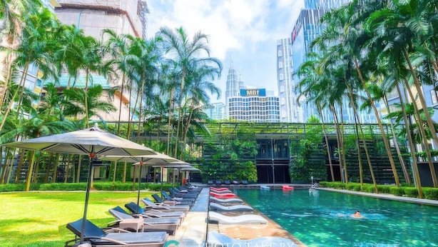 A pool area with lounge chairs and umbrellas, surrounded by palm trees and modern buildings. - St Mary Residences Luxury Apartments (Kuala Lumpur)
