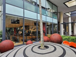 Un edificio moderno con amplios ventanales de vidrio, un árbol central y esculturas esféricas rojas.