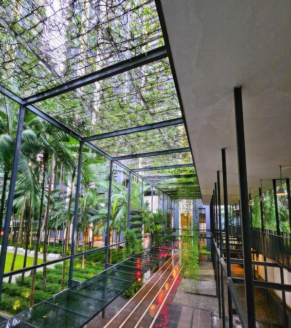 Ein modernes Atrium mit Glaswänden, einer zentralen Treppe und üppiger Bepflanzung.