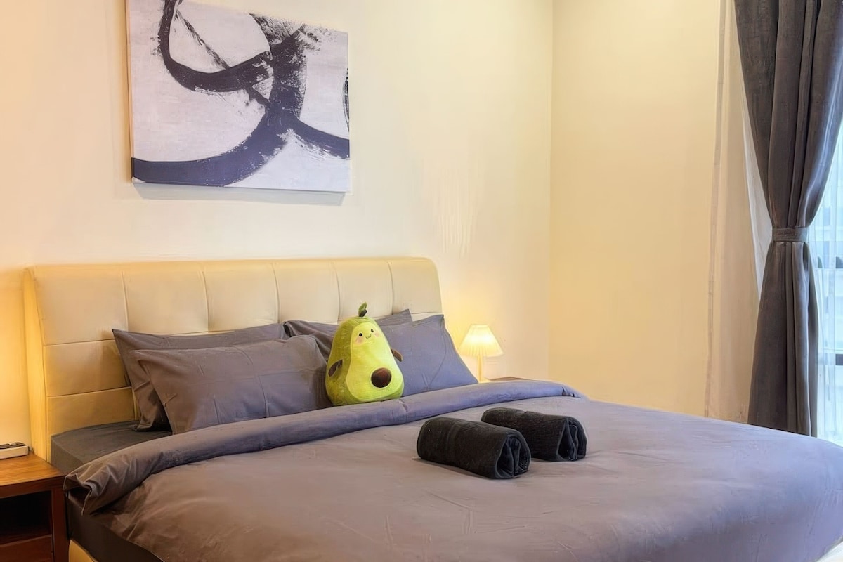 A bed with a headboard, pillows, a blanket, and a decorative pillow shaped like an avocado.