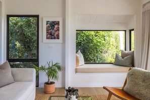 A modern living room with a sofa, a window seat, and a potted plant. - Waterfront Sanctuary, Oneroa - Now open for Christmas and New Year booking! (Waiheke Island)