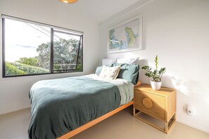 A bedroom with a bed, a nightstand, a map on the wall, and a window with a view of greenery. - Waterfront Sanctuary, Oneroa - Now open for Christmas and New Year booking! (Waiheke Island)