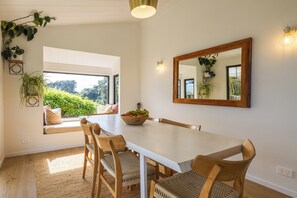 A dining area with a white table, wooden chairs, a bowl of fruit, and a large mirror on the wall.