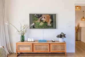 A room with a wooden console table, a framed picture of a dog, a vase with white flowers, and a potted plant. - Waterfront Sanctuary, Oneroa - Now open for Christmas and New Year booking! (Waiheke Island)