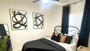 Un dormitorio moderno con una cama, un ventilador de techo, arte abstracto en la pared y una planta en maceta.