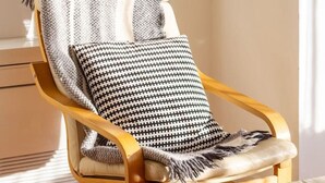 A wooden chair with a houndstooth cushion and a blanket draped over it.