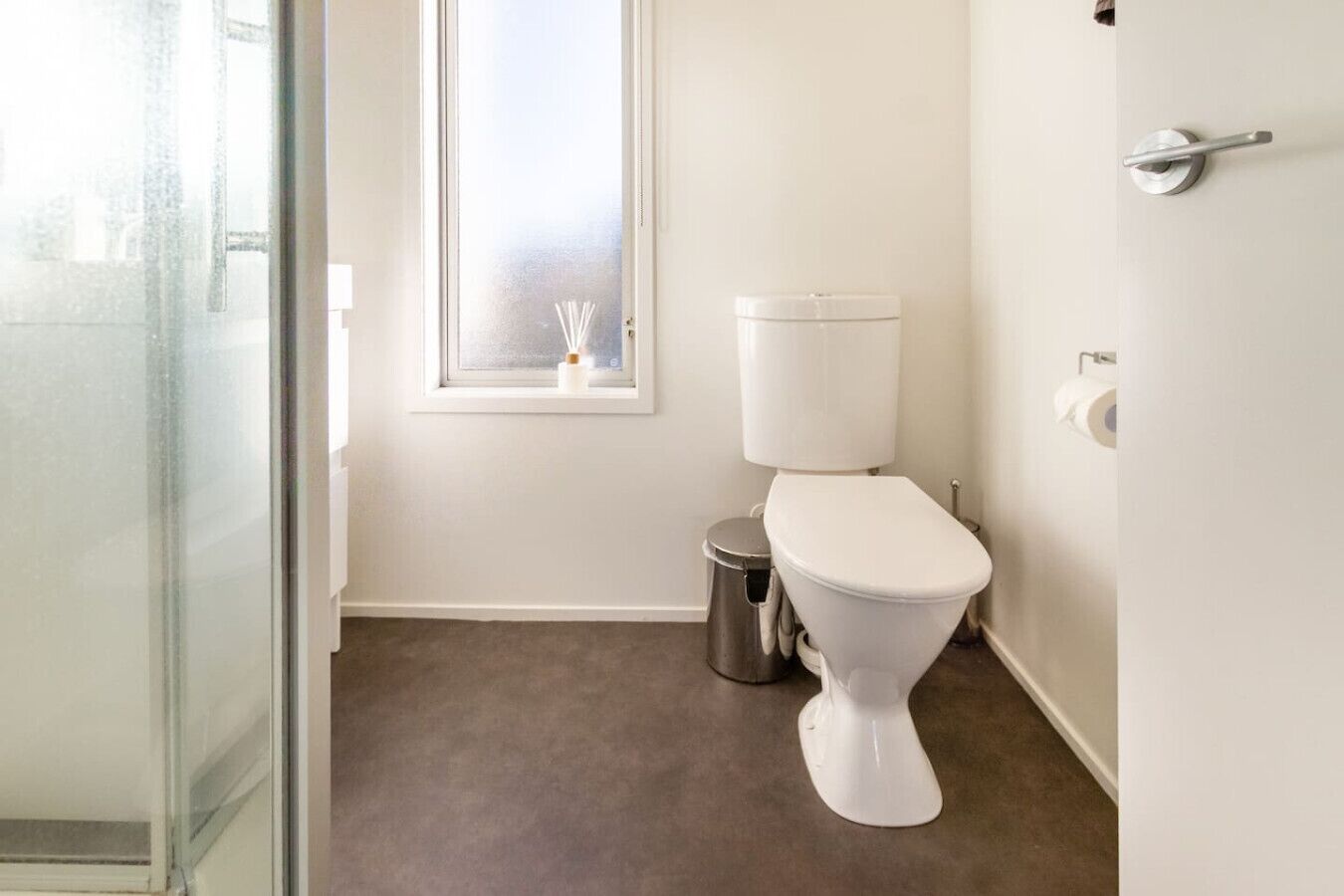 Ein kleines, sauberes Badezimmer mit Toilette, Mülleimer und Fenster.