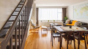 A modern living room with a dining area, a staircase, and a large window with curtains.