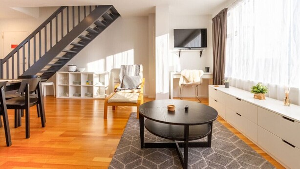 A modern living room with a staircase, a flat-screen TV, and a dining area.