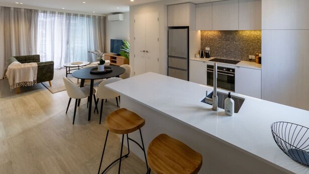 A modern kitchen with a central island, a dining area with a round table, and a living space with a sofa and a TV. - Luxe Central City 2 bedrooms with Carpark (Christchurch)