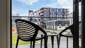 A view from a balcony with two chairs and a table, overlooking a modern building complex with multiple balconies and a clear sky. - Luxe Central City 2 bedrooms with Carpark (Christchurch)