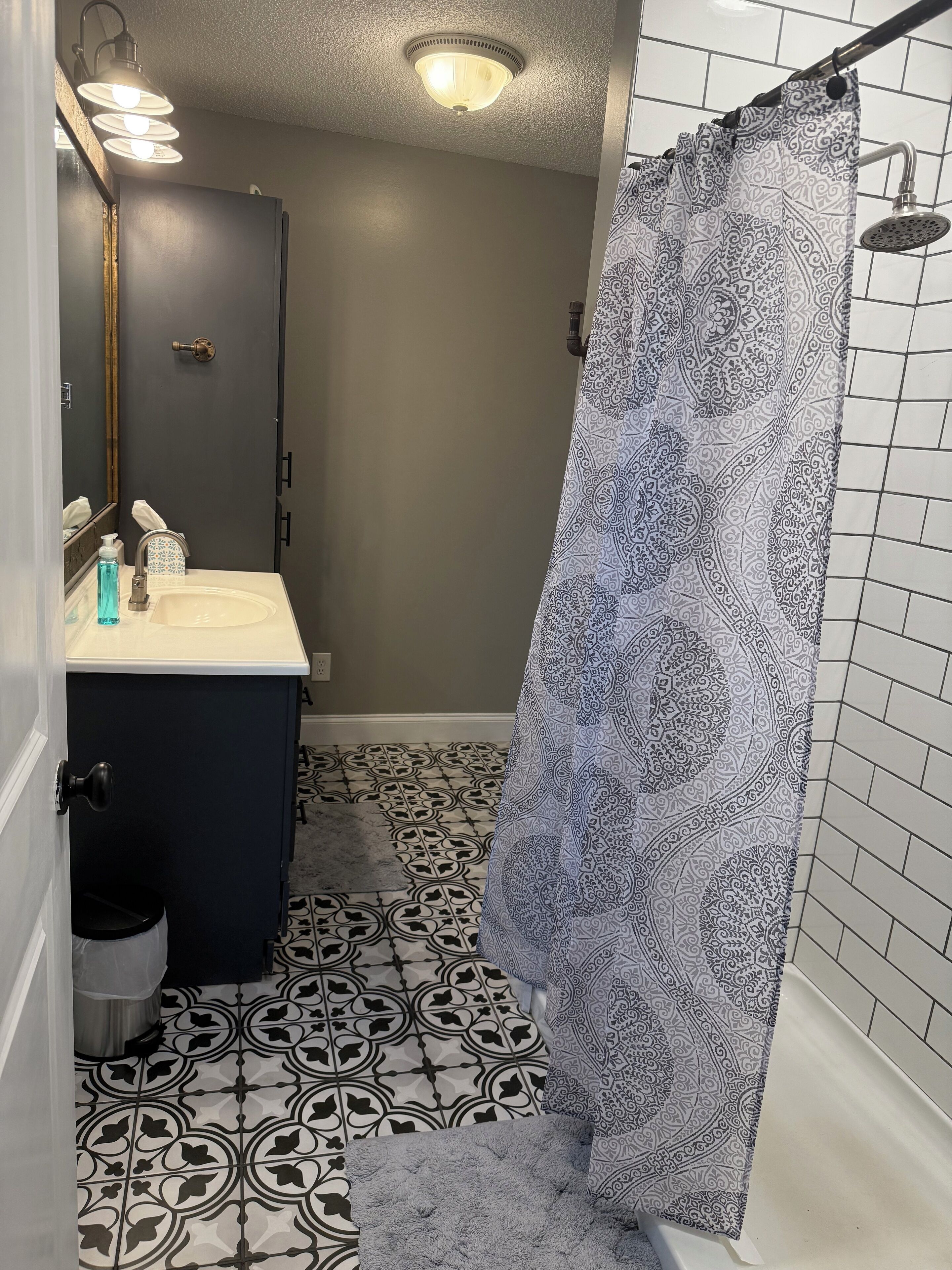Ein Badezimmer mit einem gemusterten Duschvorhang, einem Waschbecken mit Spiegel und einer Toilette.
