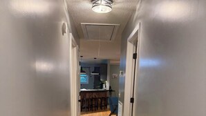 A hallway with wooden flooring, a ceiling light, and a kitchen area visible in the background. - Charming 3-bedroom house with WiFi and AC in beautiful Loretto (Loretto)