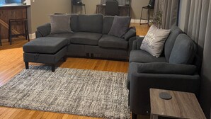A living room with a sectional sofa, a small table, a ceiling fan, and a rug. - Charming 3-bedroom house with WiFi and AC in beautiful Loretto (Loretto)