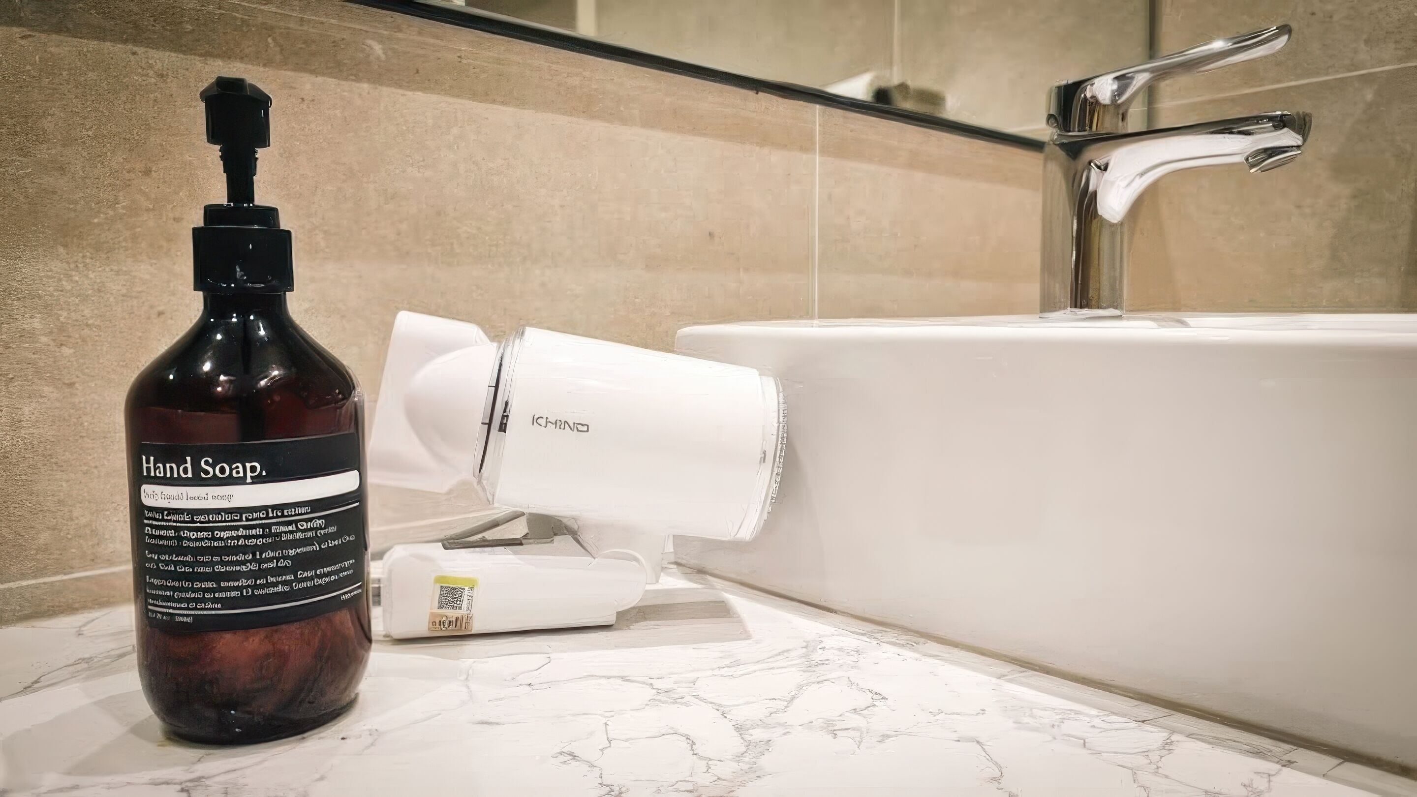 A bottle of hand soap and a white hairdryer on a bathroom counter next to a bathtub.
