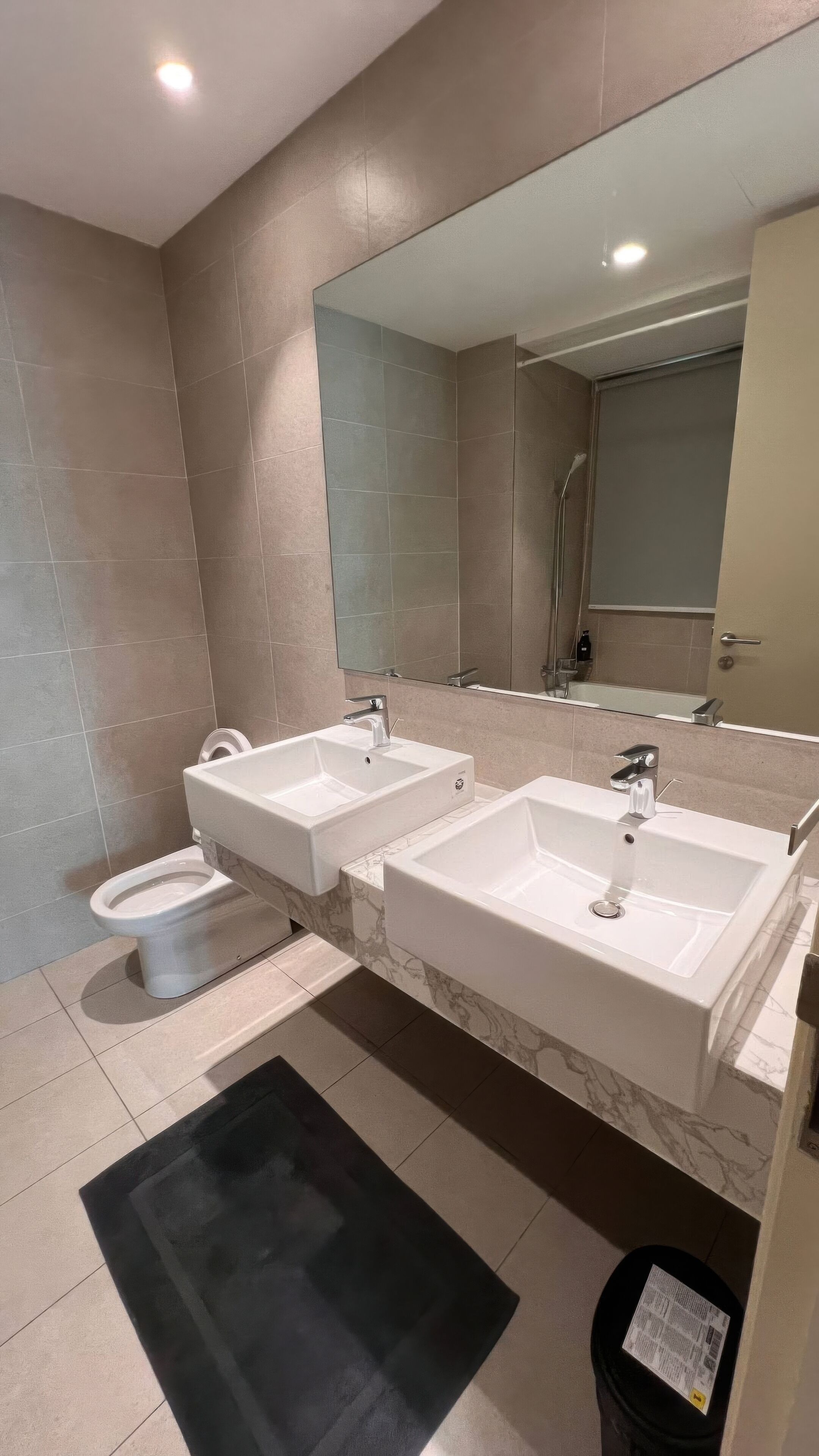 A modern bathroom with two sinks, a toilet, and a large mirror.