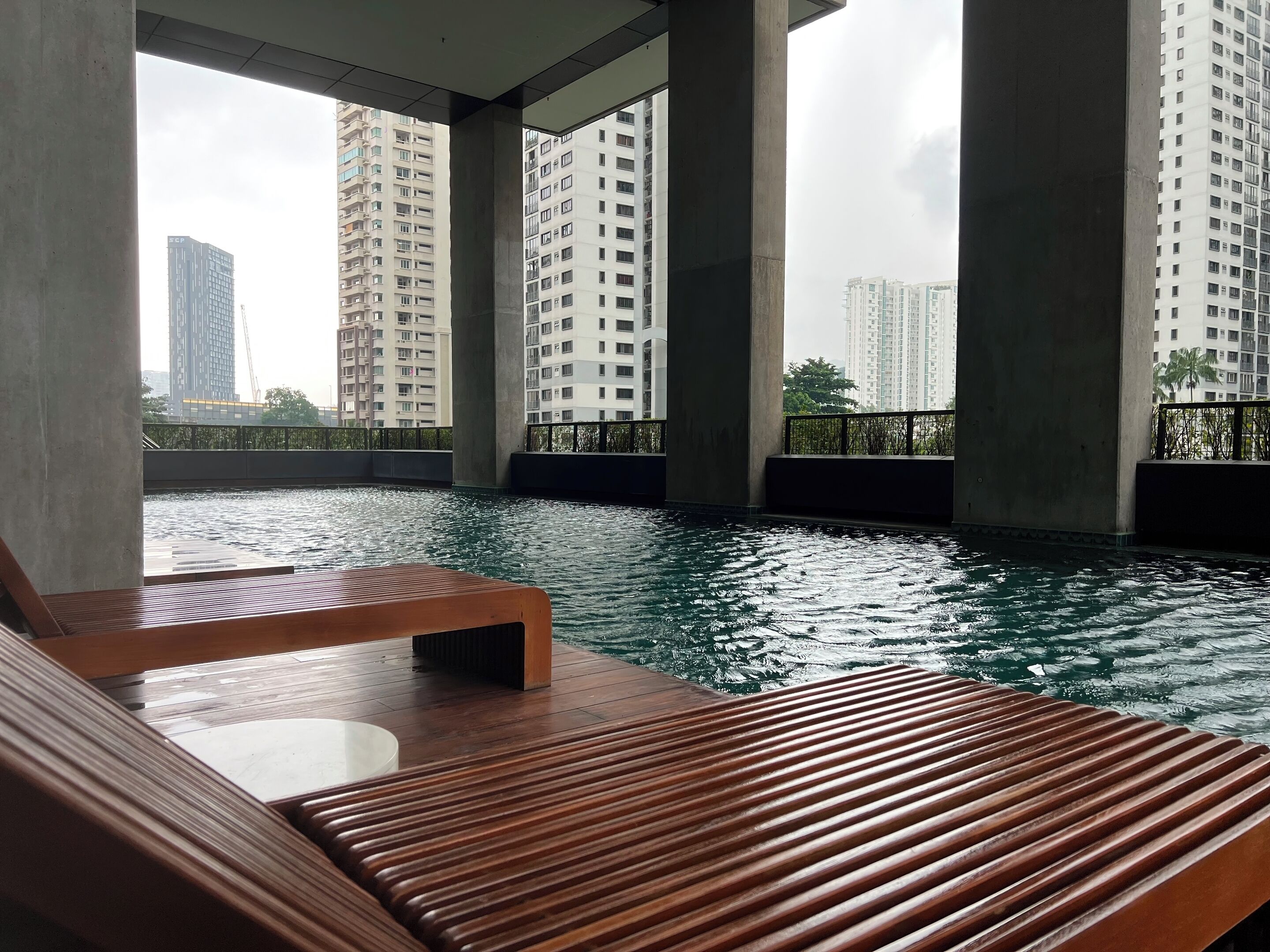Un espace piscine avec des chaises longues en bois et une vue sur les immeubles de grande hauteur.