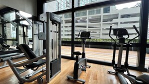 Un gimnasio con equipo de ejercicio, ventanas amplias y vistas a un estacionamiento.