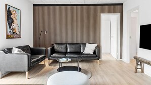 Una sala de estar moderna con un sofá de cuero negro, una mesa de centro redonda y una pared de listones de madera.