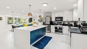A modern kitchen with white cabinets, a central island, stainless steel appliances, and pendant lighting. - Luxurious 7-bedroom villa with pool/spa and pickleball court in fabulous Naples (Naples)