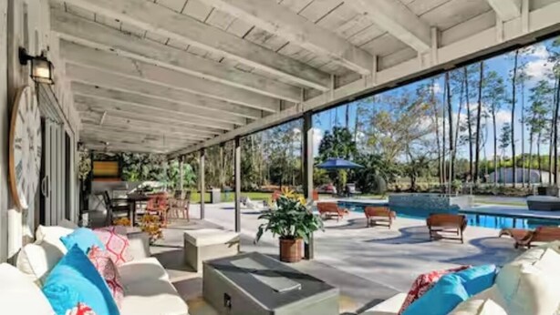 A covered outdoor seating area with white sofas, a fire pit, and a pool in the background. - Luxurious 7-bedroom villa with pool/spa and pickleball court in fabulous Naples (Naples)