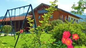 Een houten huis met een balkon, omringd door een tuin met rozen en een schommel.