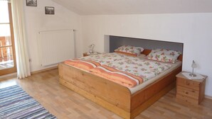 Een slaapkamer met een houten bed, een nachtkastje, een radiator en een raam met gordijnen.