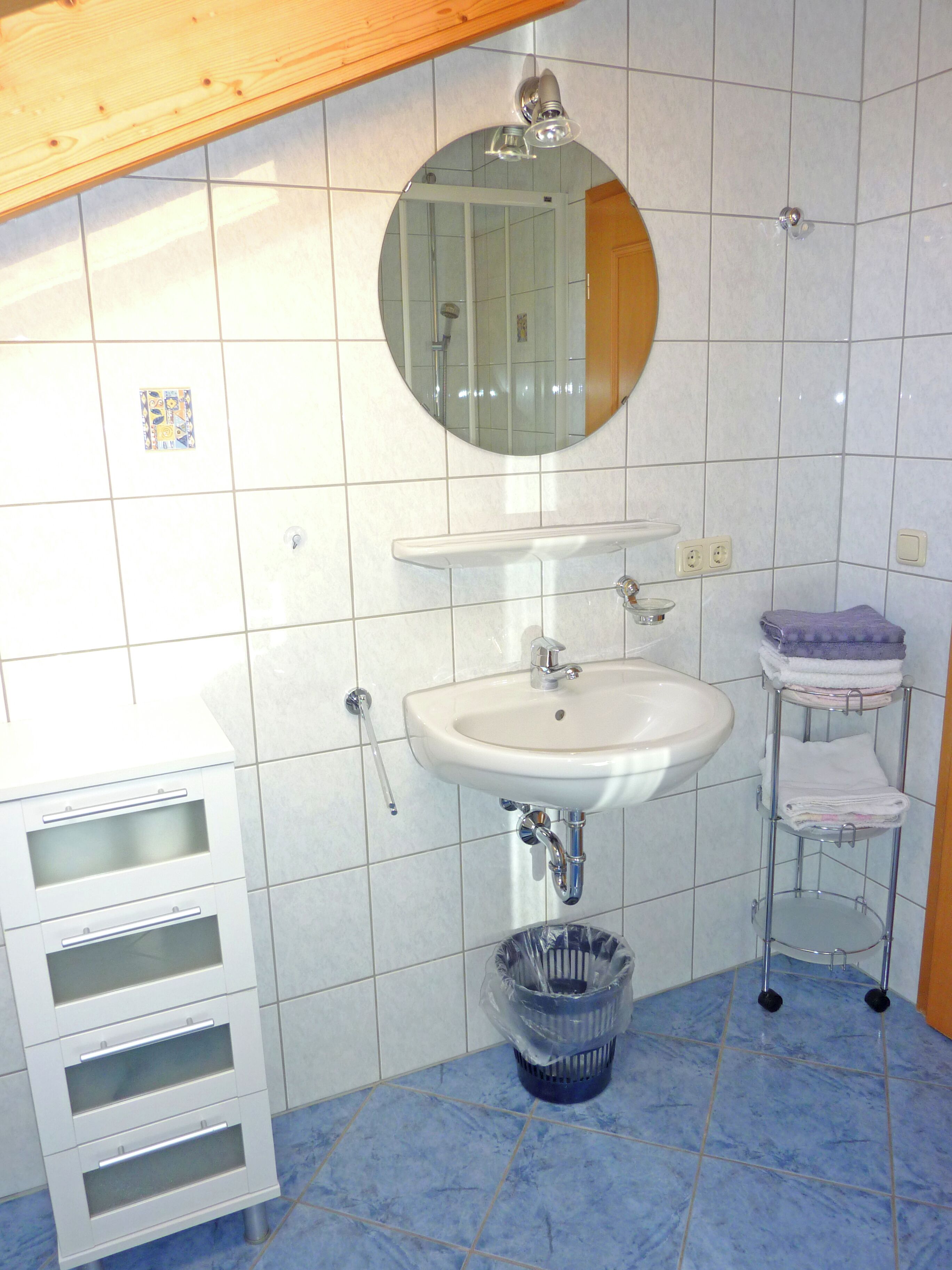 Een badkamer met een wit wastafelmeubel, spiegel en een vloer van blauwe tegels.