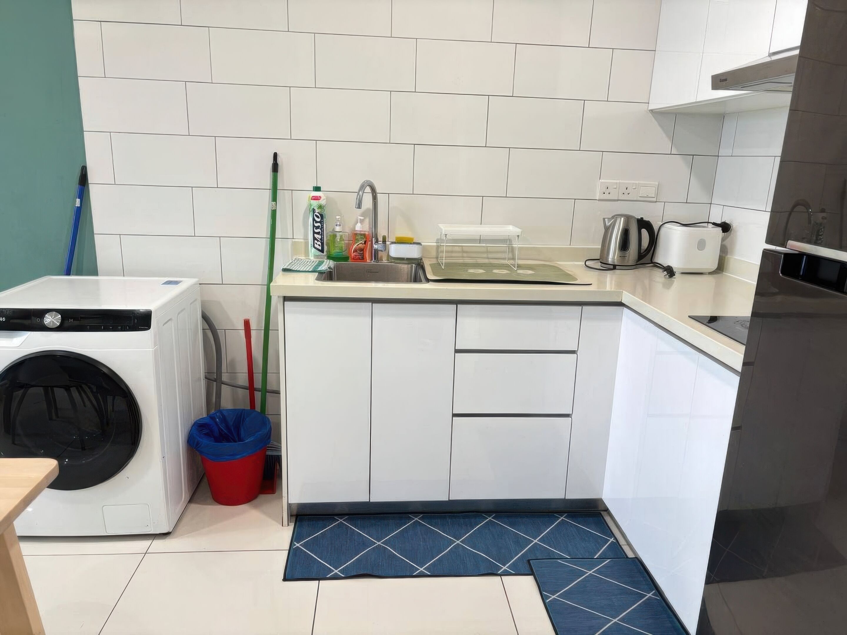 A compact kitchen with a washing machine, a sink, and a kettle.