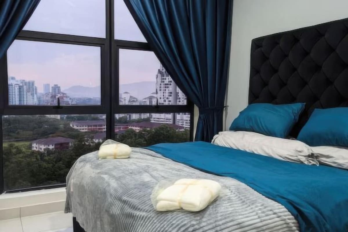 A bedroom with a large window, a tufted headboard, and two pillows on the bed.