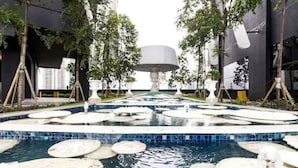 Ein moderner Außenpoolbereich mit kreisförmigen Wasserspielen und einer zentralen Fontäne, umgeben von Bäumen und moderner Architektur.